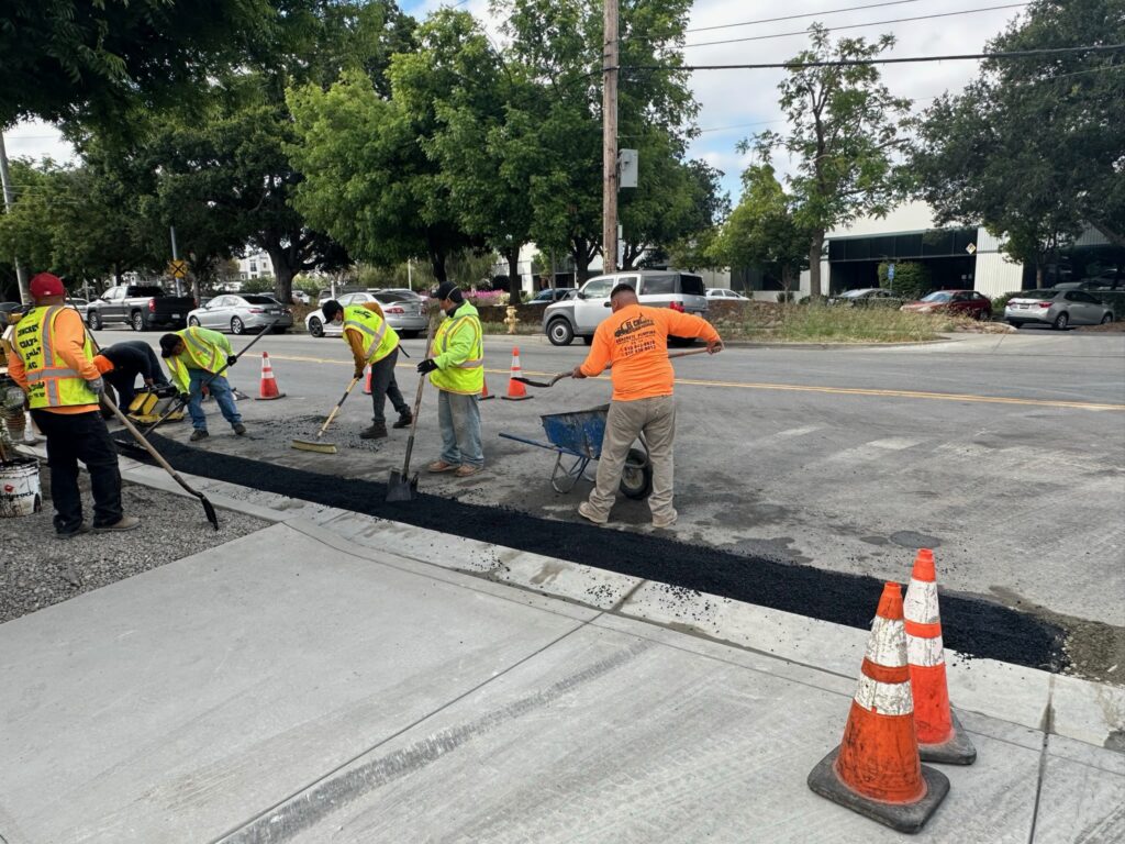 Asphalt repair and patching crew laying hot asphalt along a curb in the South Bay Area